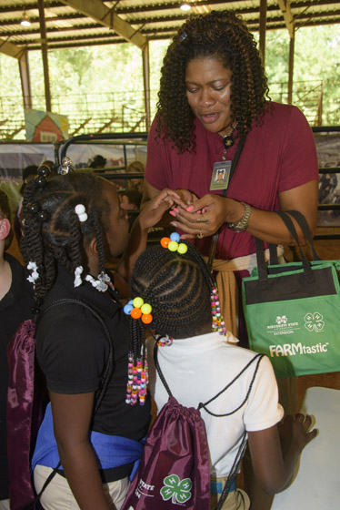A woman holding a green FARMtastic bag talks to two young girls.