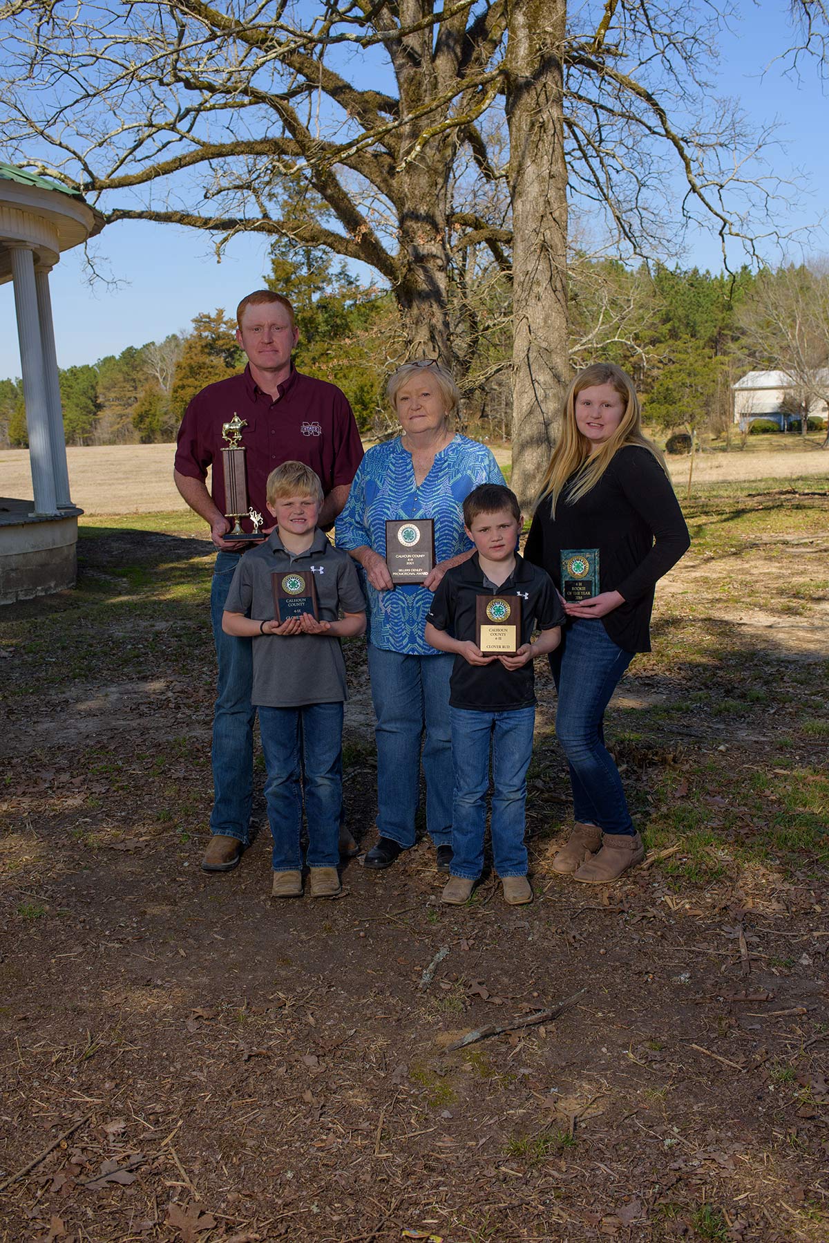 An older woman, man, young girl, and two young boys stand together, each holding a plaque.
