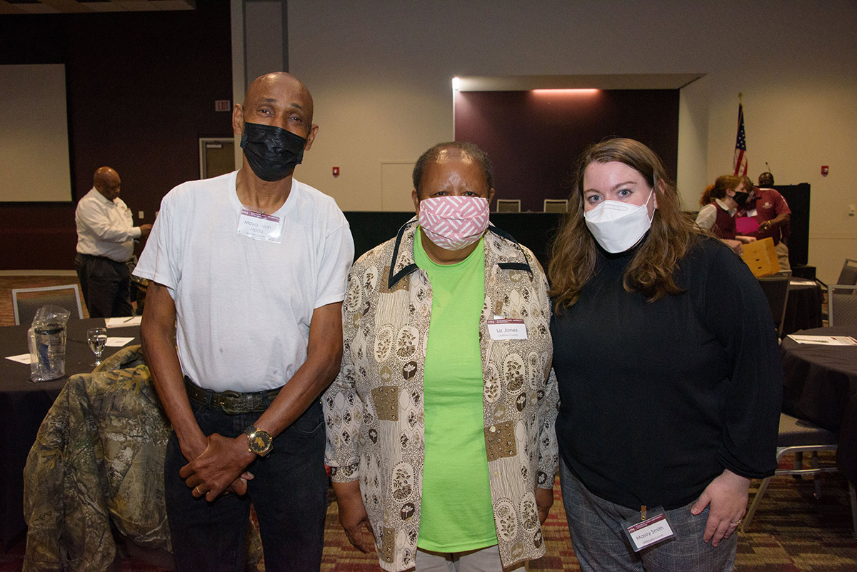 Three people wearing masks stand together for a photo.