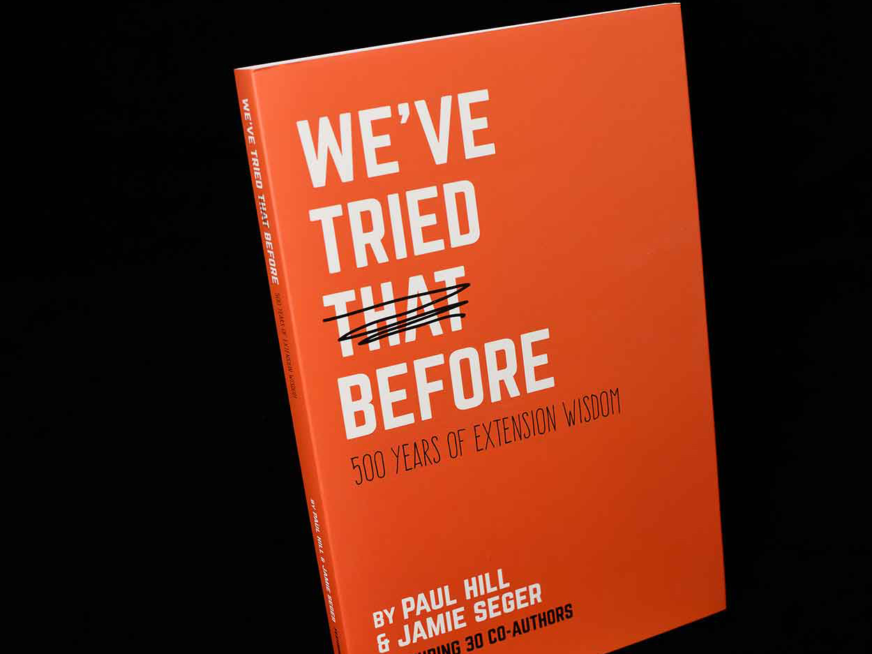 An orange book lies on a black background; the cover of the book, in white, reads, “We’ve Tried That Before: 500 Years of Extension Wisdom.”