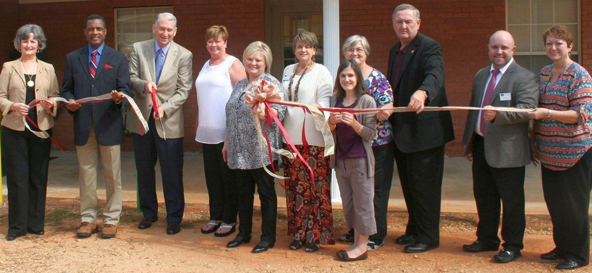 Seven people holding the right side of a cut ribbon with one man in a suit holing large scissors with two others to the left holding the shorter end of the cut ribbon.