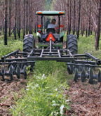 A tractor pulls a disking implement through an open area in a forest.