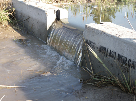 A check dam, or concrete structure placed across the width of a drainage ditch to control the flow of water off of an agricultural field. Water pours over the center, lower portion of the dam.