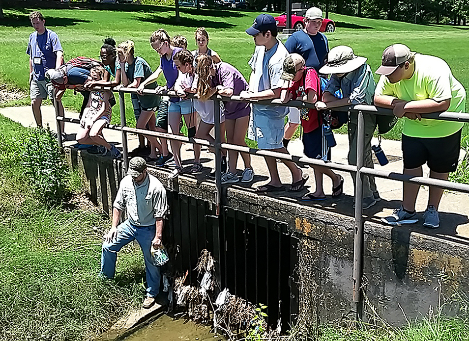 A large group of people stands at a railing overlooking a stream of water.