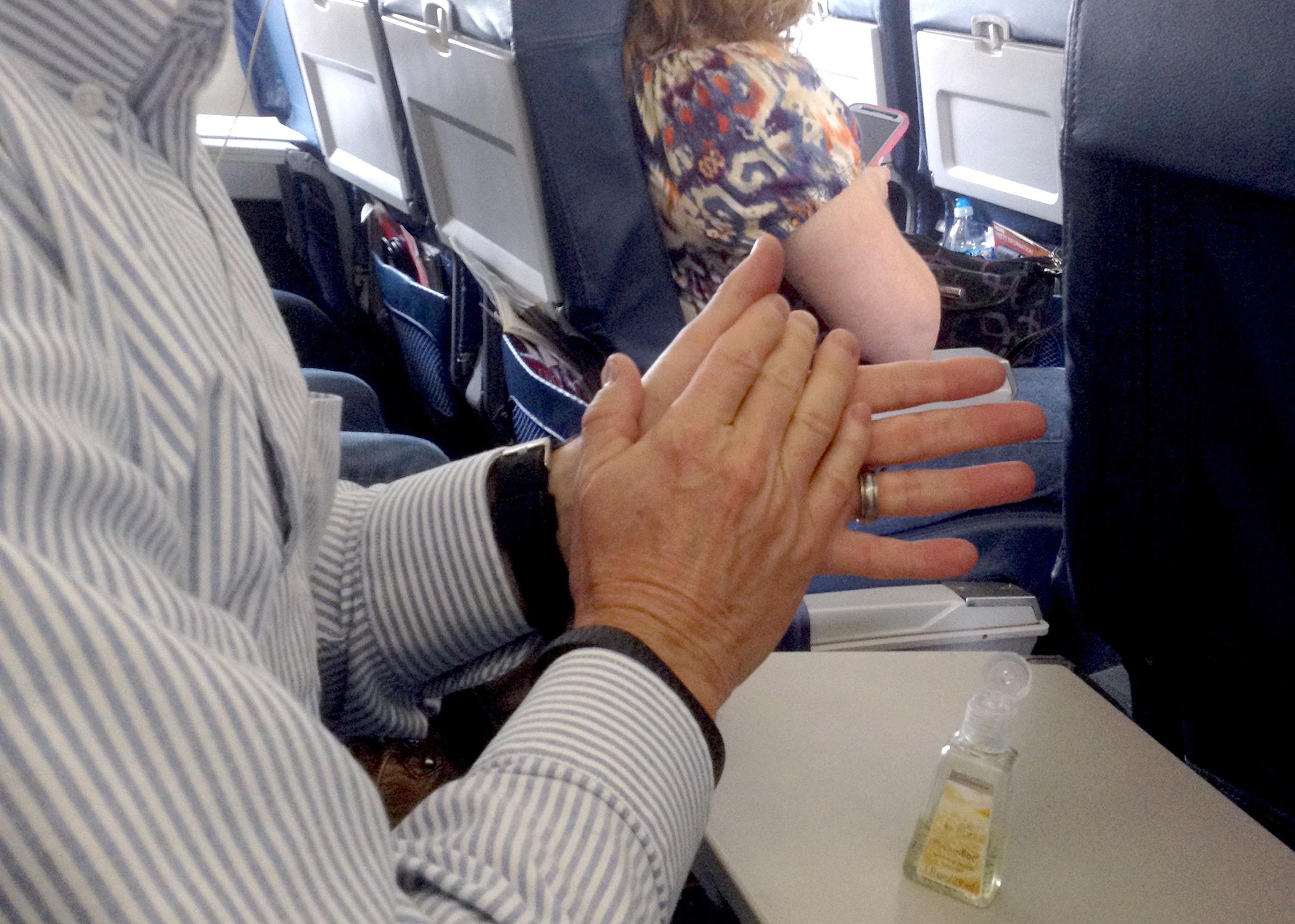 man washing hands with alcohol-based rub seated in airplane.