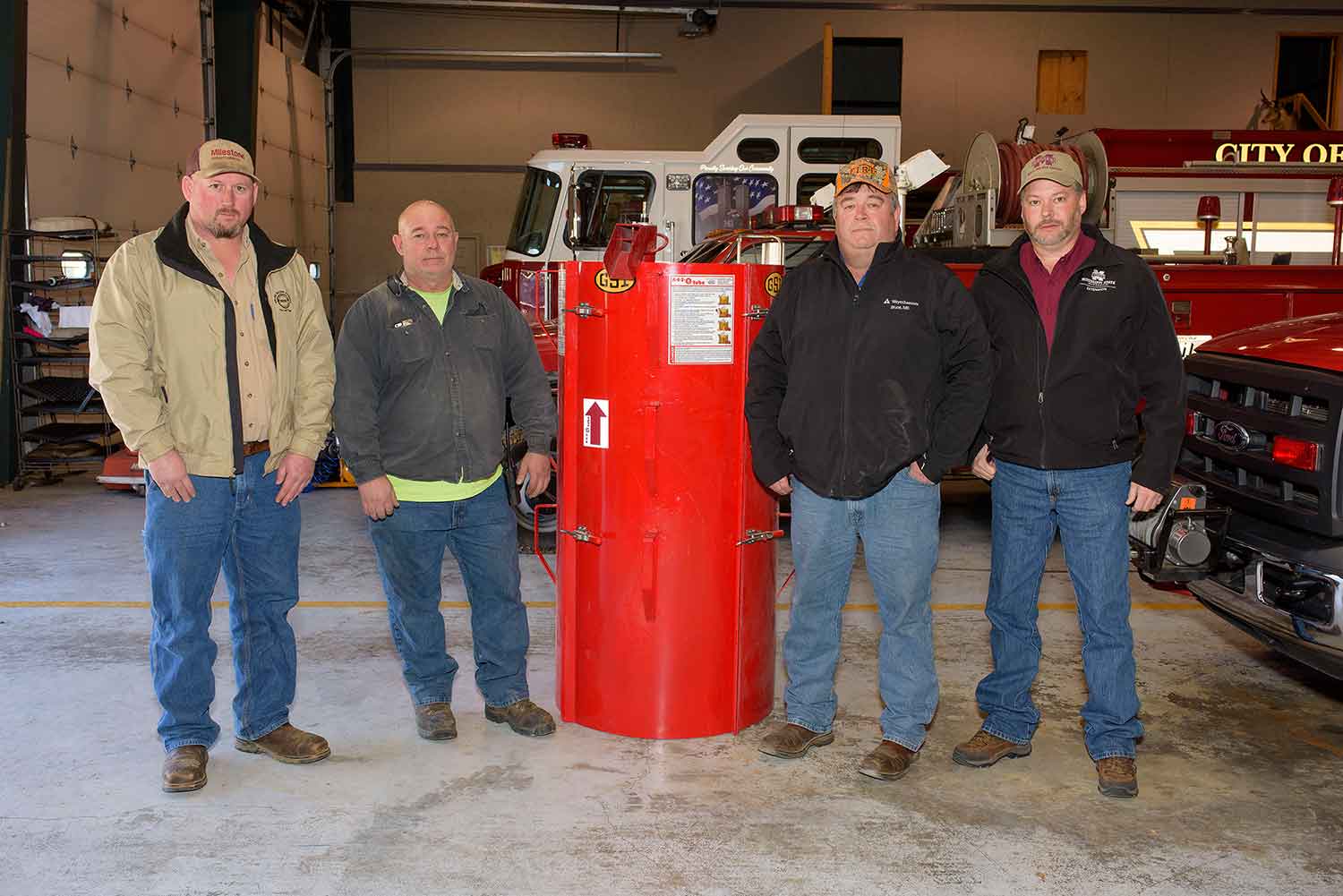 Four men stand in front of a red firetruck.