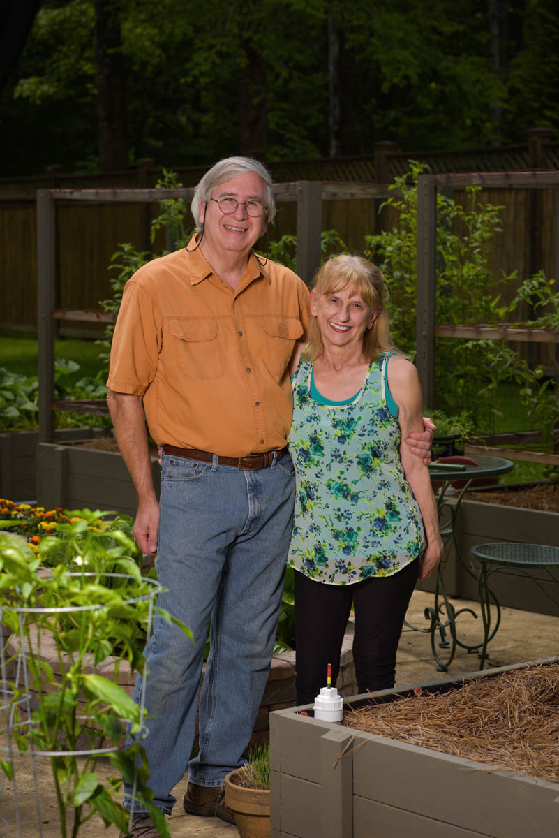 A man wearing an orange shirt stands with his arm around a woman wearing a blue floral tank top.