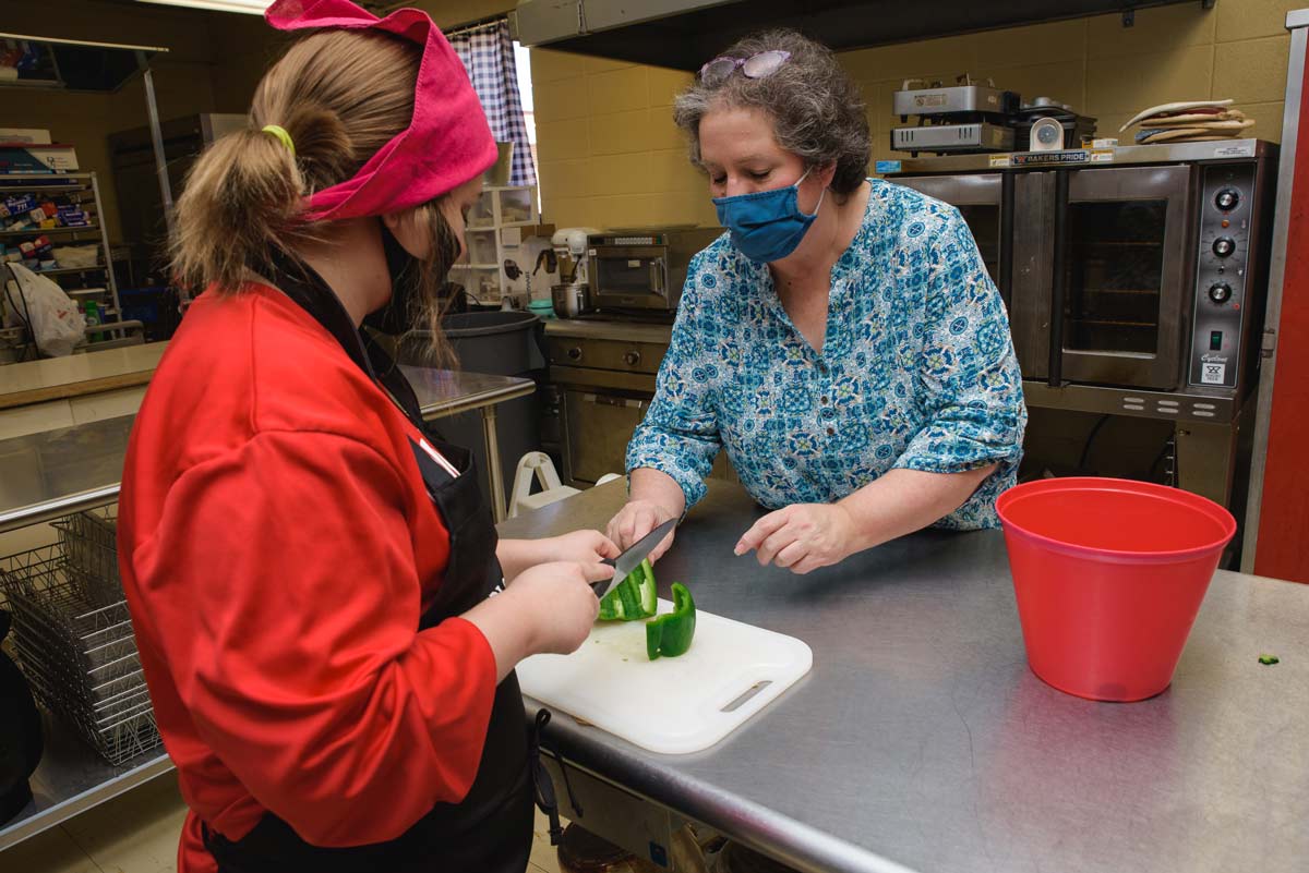 A female teen chopping a green bell pepper with an older woman looking on.