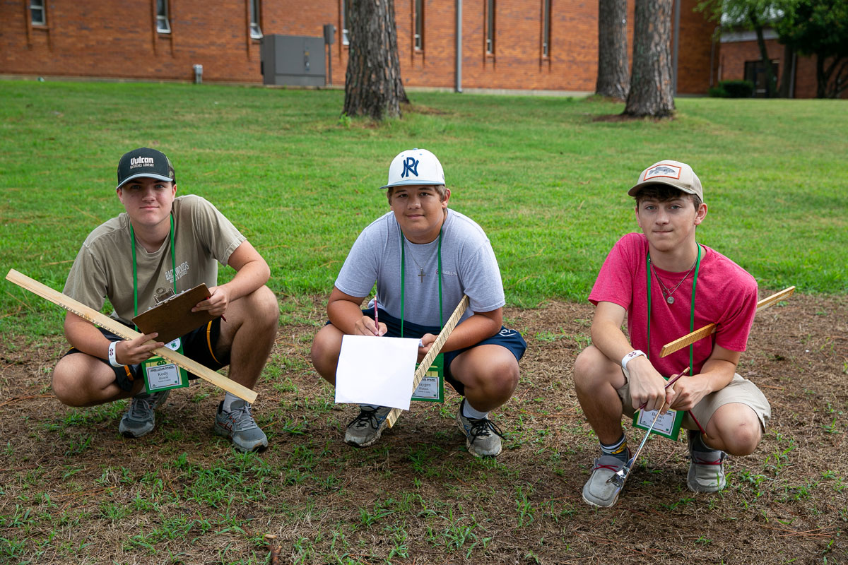 Three young men squatting on grass smile for a group photo.