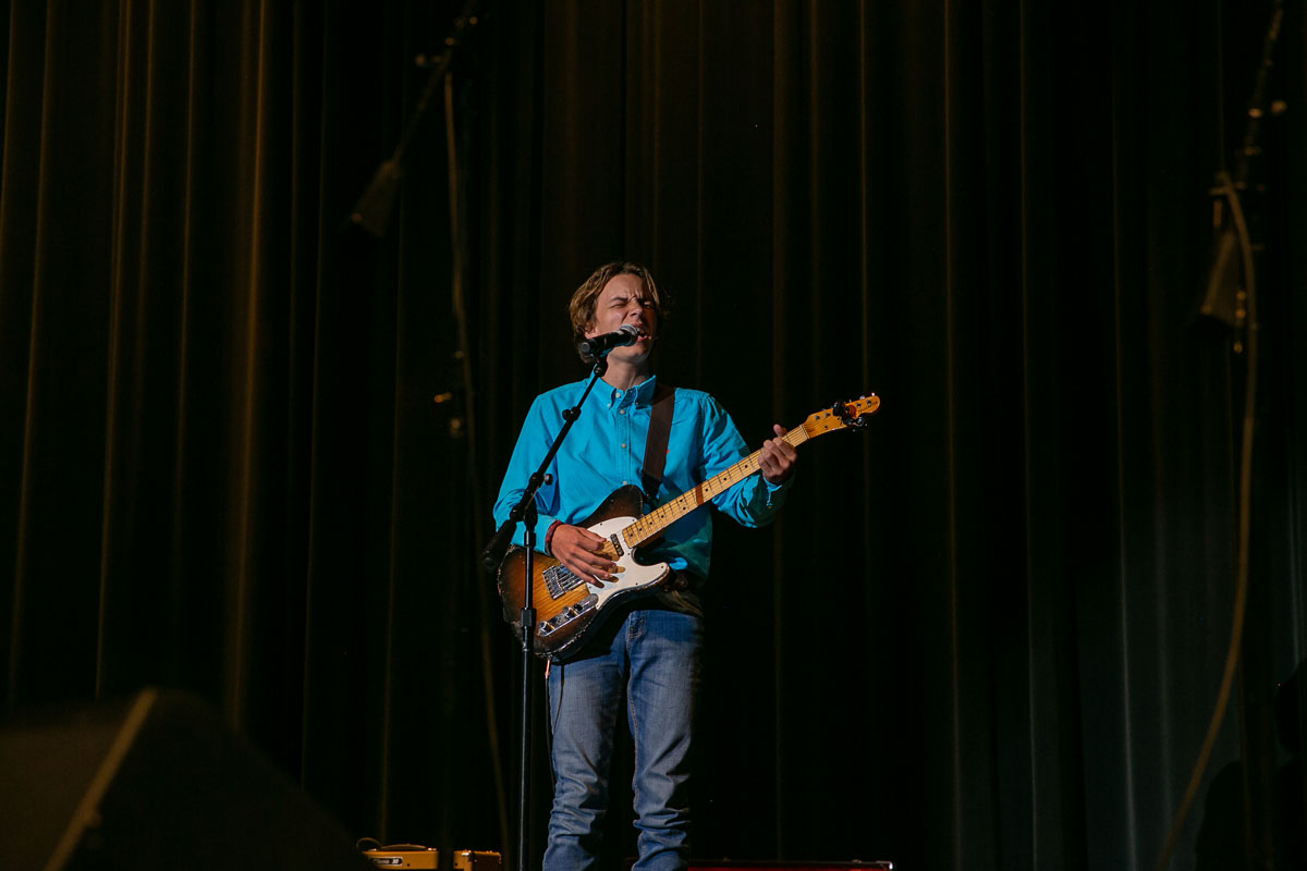 A teenage boy singing into a microphone and playing guitar.