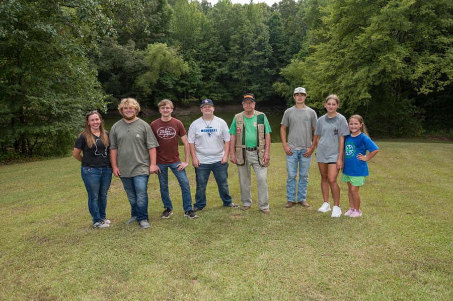 : A group of people standing in a line outside and smiling.