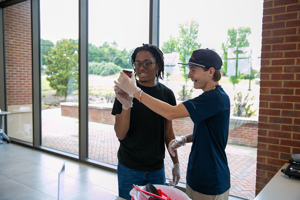 Two teens wearing gloves examine a jar.