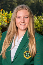 A blonde girl wearing a green jacket and khakis, smiling.