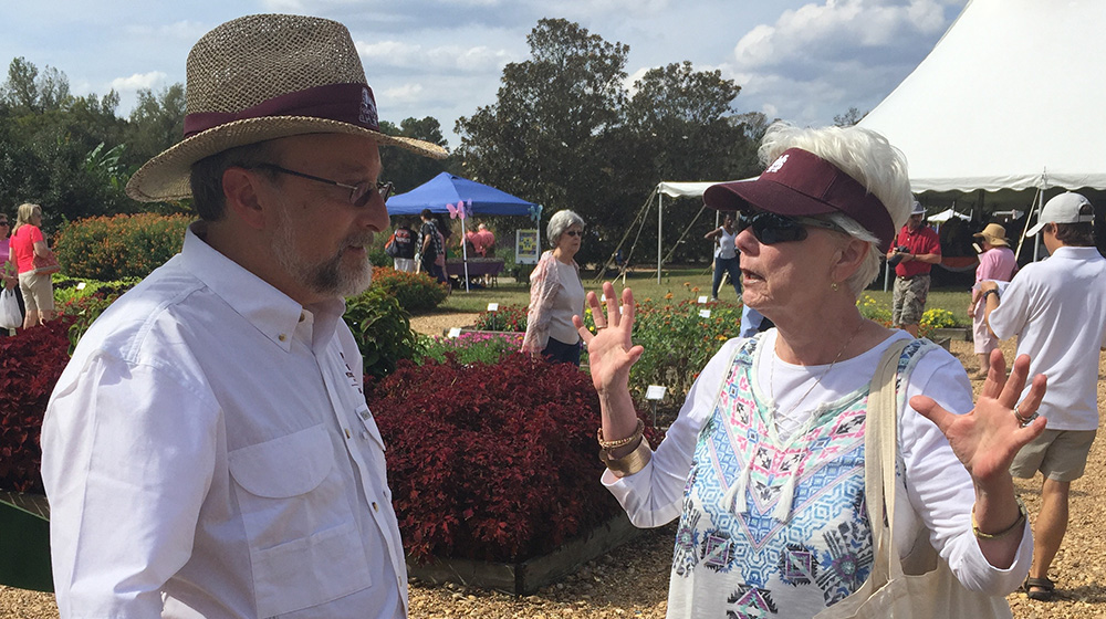 Extension specialist talks with a woman in a raised bed flower garden during an outdoor gardening seminar