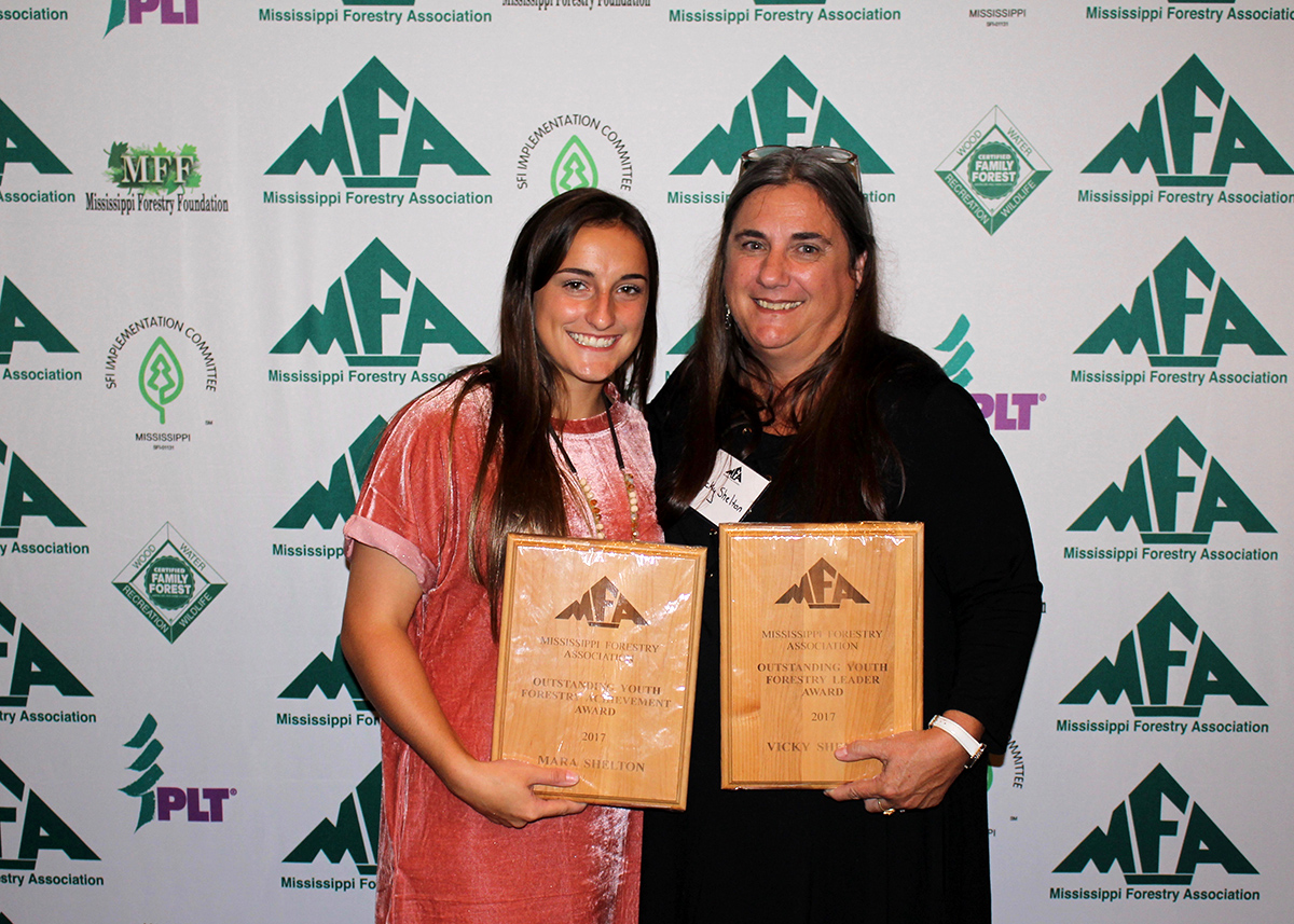 Two women stand while holding award plaques at the Mississippi Forestry Association annual meeting. 
