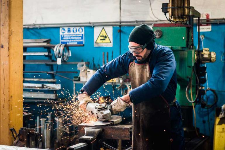 A man in protective goggles and gloves working in a factory setting