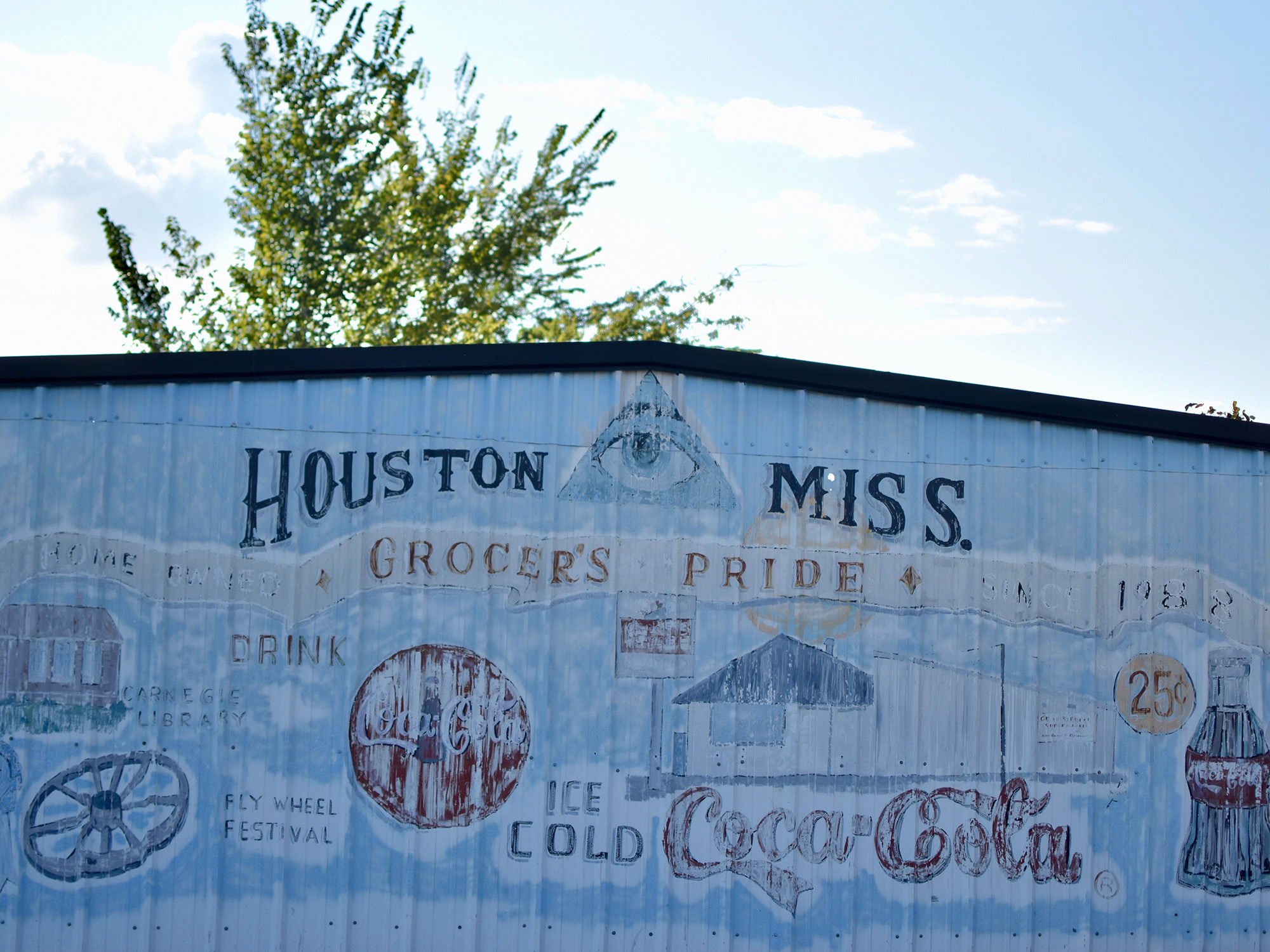 Photo of the side of a metal building that has been painted blue and has several different symbols and paintings.