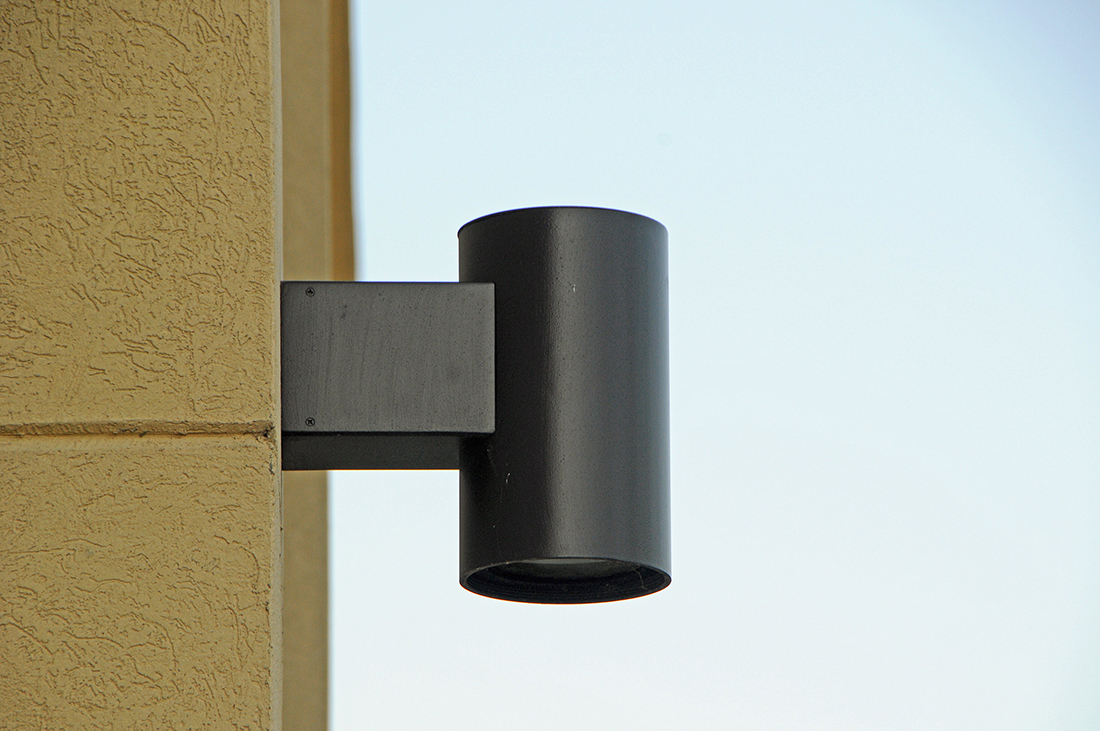 A dark metal exterior light mounted on the side of a beige building.