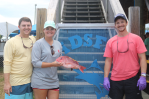 A woman holding a red snapper with 2 men on either side.