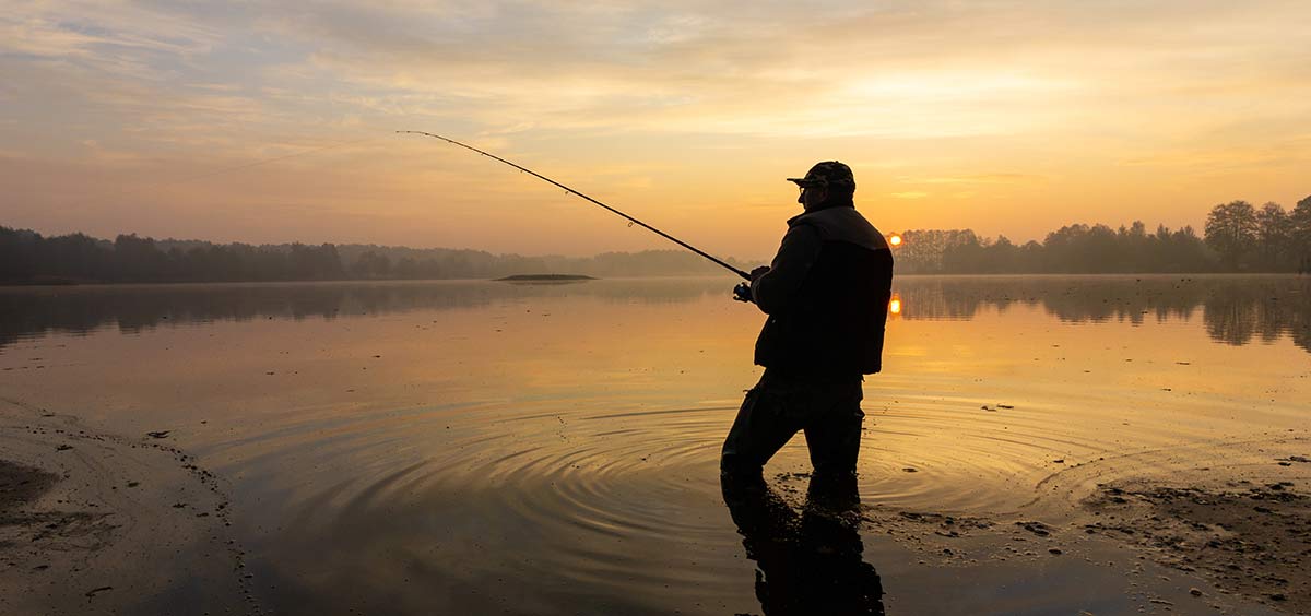 Man fishing in water at sunset.