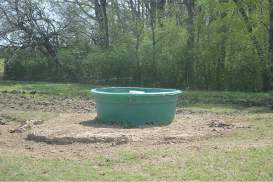 A water trough on a concrete slab with a silver float in the middle. 