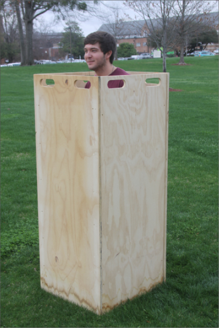 A man standing in a plywood box with handles at the top.
