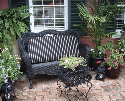 Bamboo palms and several other plants on an outdoor patio with a cushioned bench.