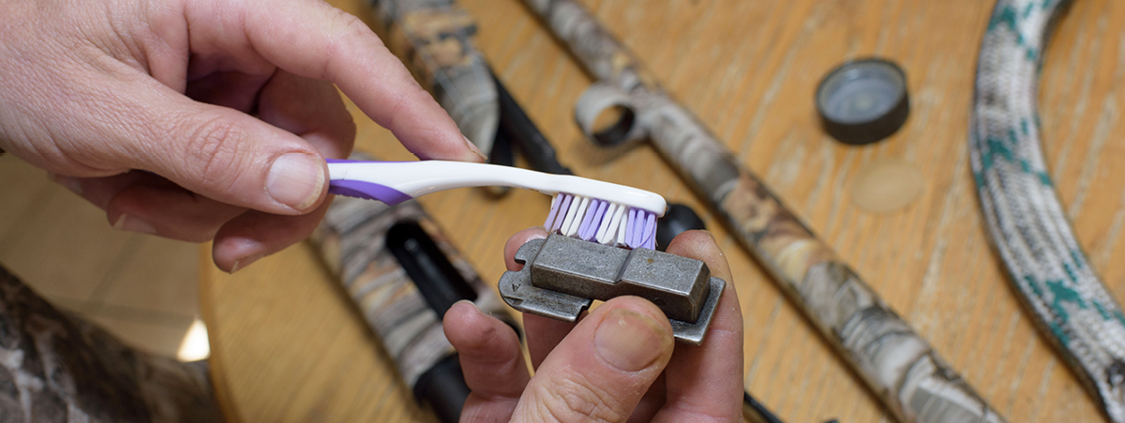 Cleaning a gun part with a toothbrush.