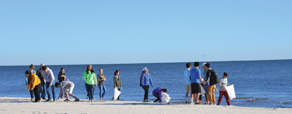 A group of people pick up debris on a coastal beach.