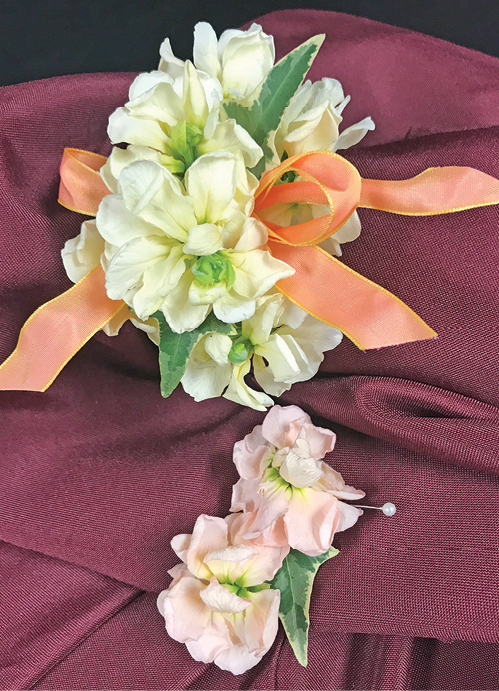 A corsage of white flowers with a peach-colored bow, and a small boutonniere of two light pink flowers.