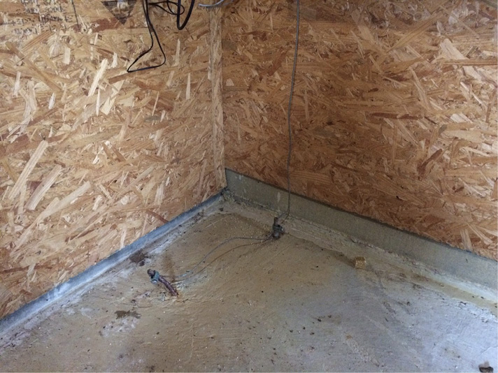 A corner of a building with a concrete floor and plywood walls. The rebar and ground rod are coming out of the concrete floor.