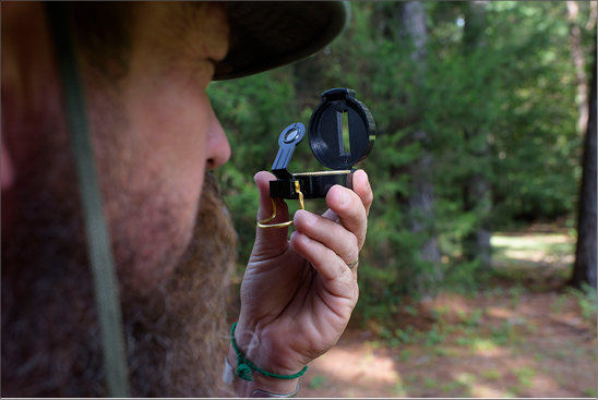 A person holds a compass up and peers through it at an object in the distance.