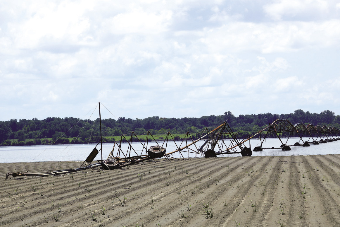 A partially flooded farm field contains damaged irrigation equipment.