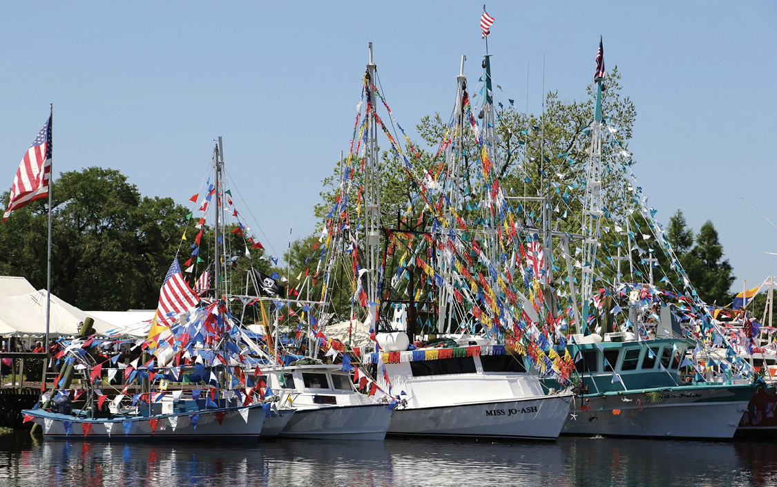 Four fishing boats covered in decorative flags in a harbor.