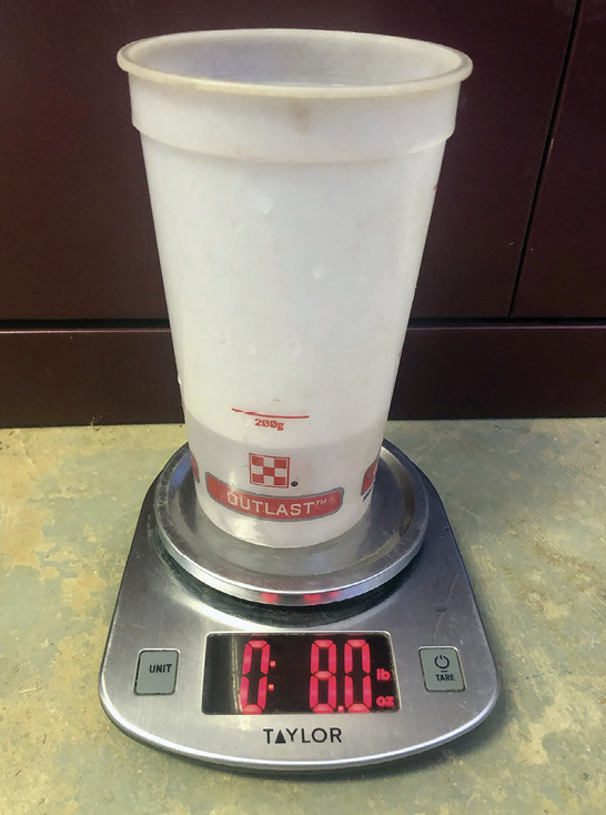 A plastic cup holding a small amount of oil is weighed on a scale.