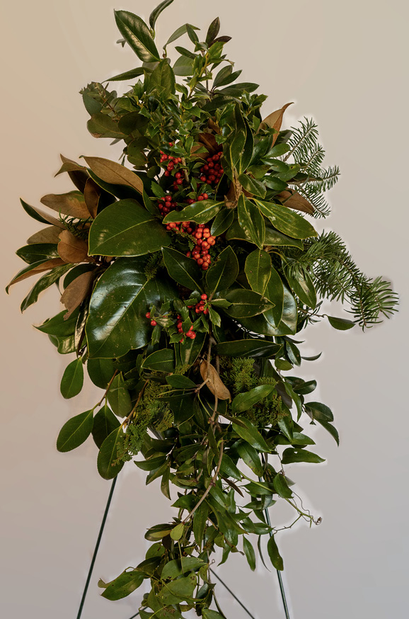 An arrangement of magnolia leaves and other greenery and red berries displayed on a wreath stand.