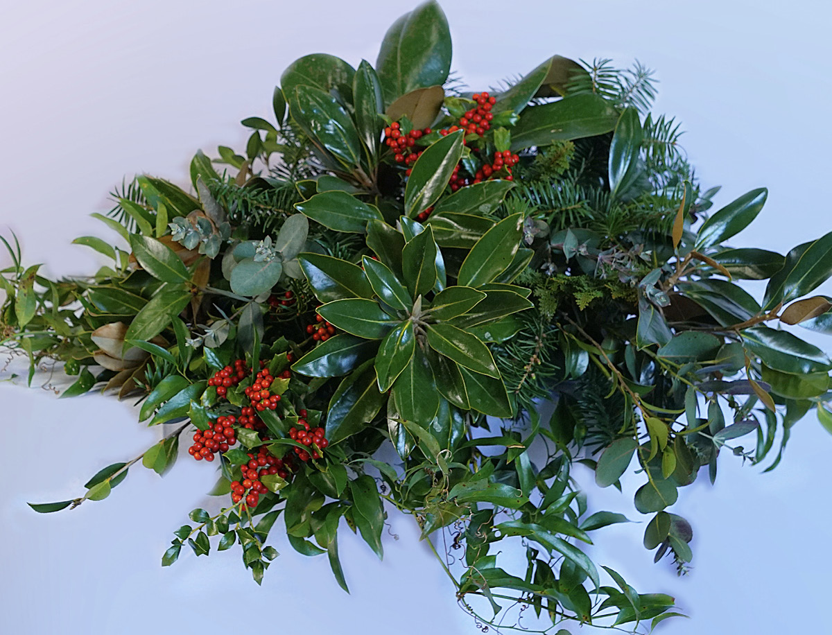 An arrangement of magnolia leaves and other greenery and red berries.