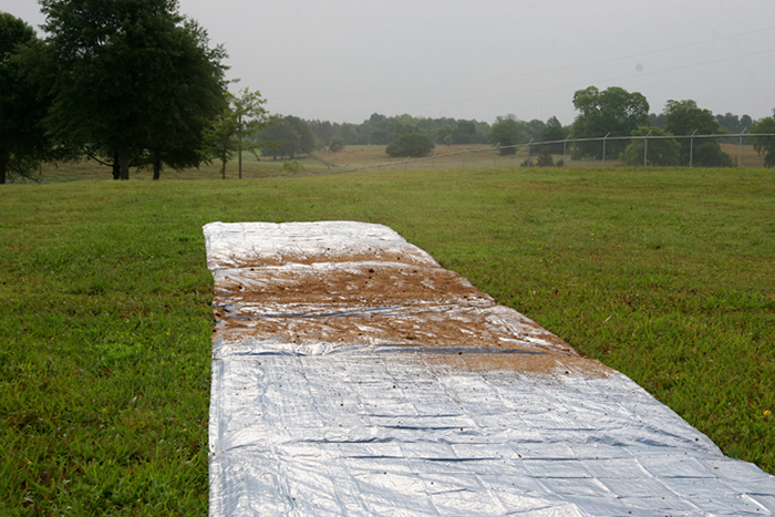A tarp spread with poultry litter n a green field.