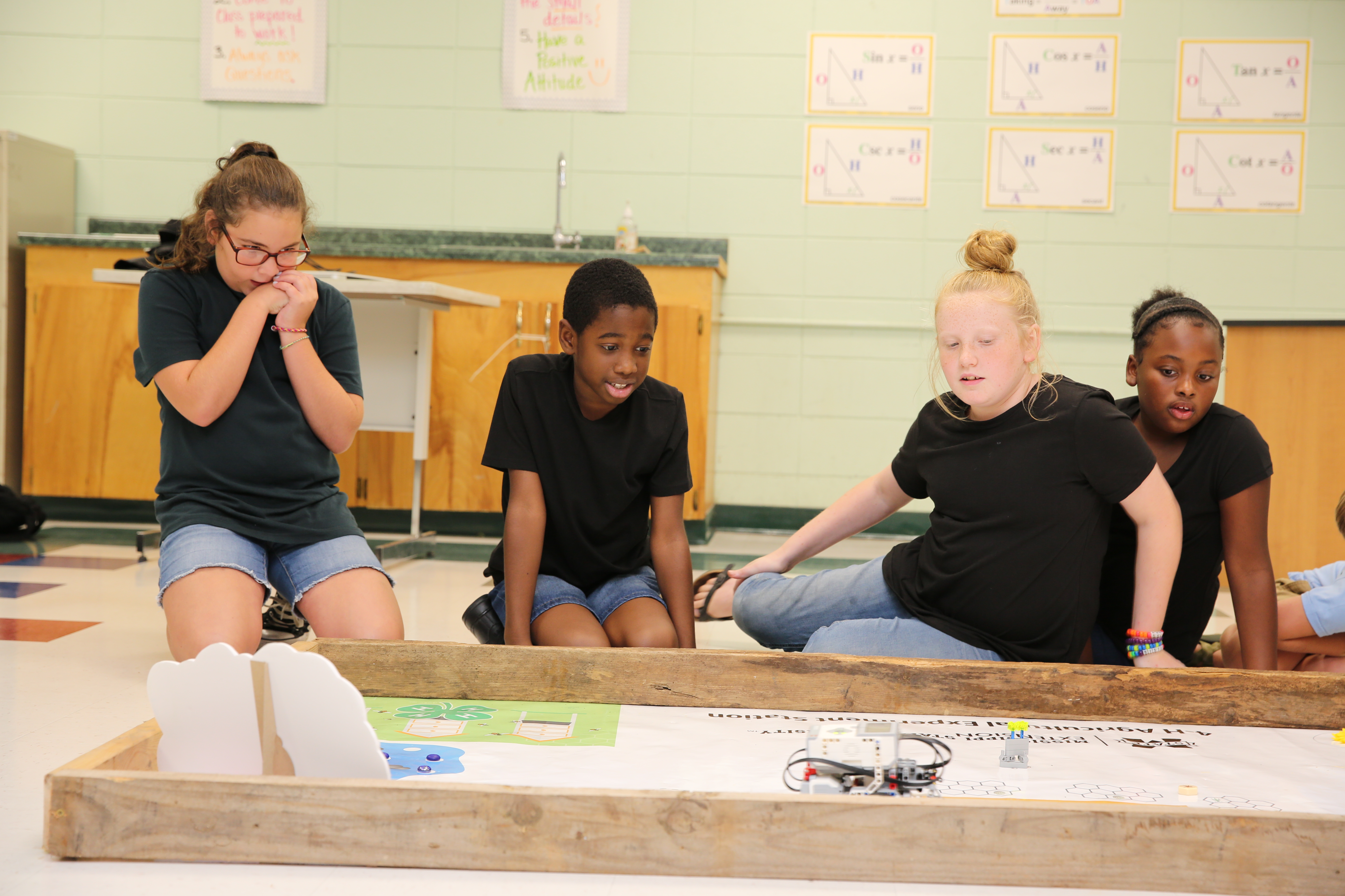Three girls and one boy wearing black shirts looking anxious as they compete in a robotics competition.