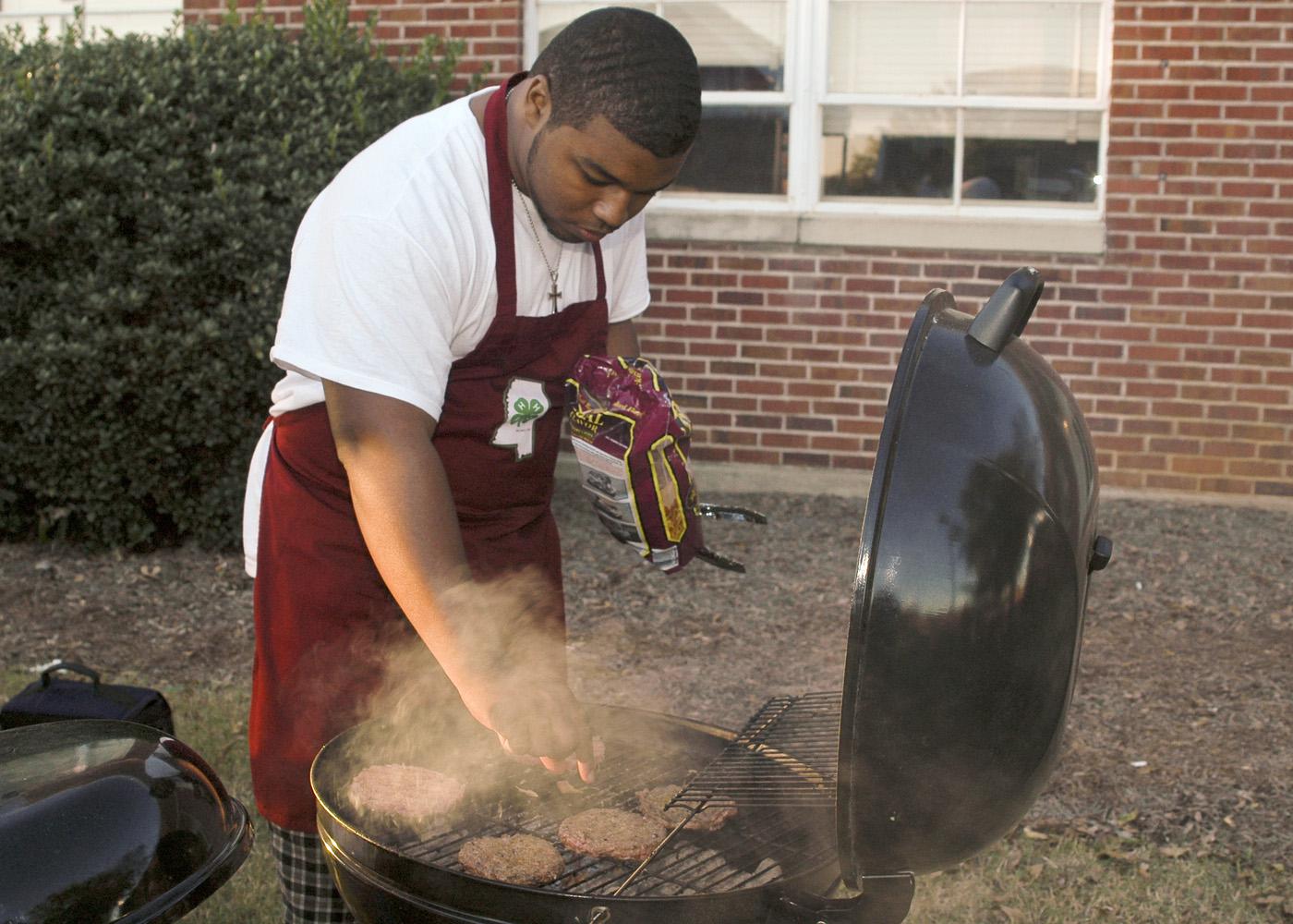 Mississippi State University Collegiate 4-H member Billy Hudson, 19, of Greenwood tries his hand at grilling during one of the club's recent football tailgates. While club members often get together to socialize, they make community service a priority. (Photo by Patti Drapala)