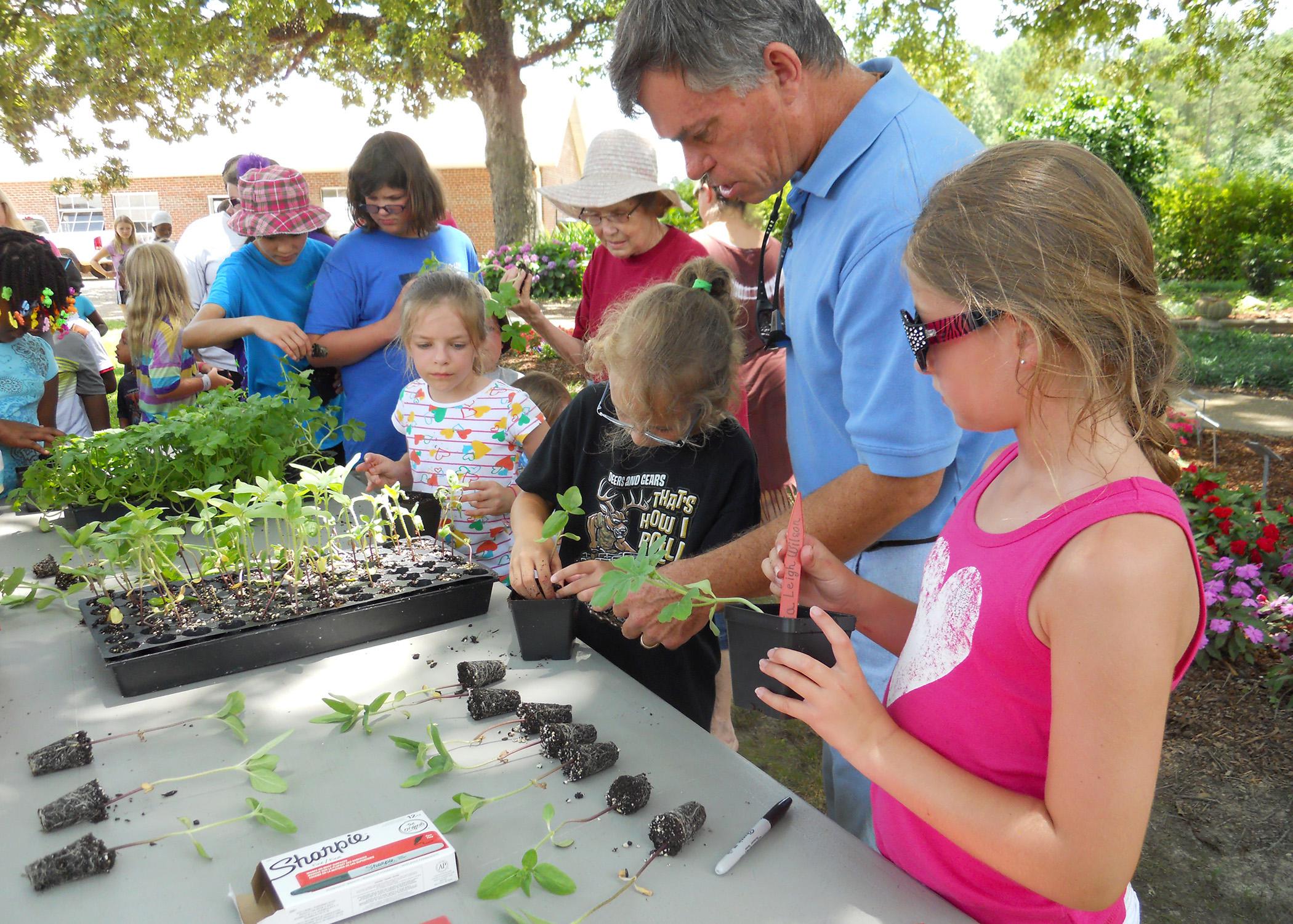 Bill Evans, center, helps Bayleigh Newman, left, and Olivia Leigh Williams, right, plant their watermelon seedlings at Mississippi State University's Truck Crops Station June 12. Employees at the station held a short program on gardening to complement the Dig into Reading theme of this year's statewide library summer reading program. (Photo by MSU Ag Communications/Susan Collins-Smith)