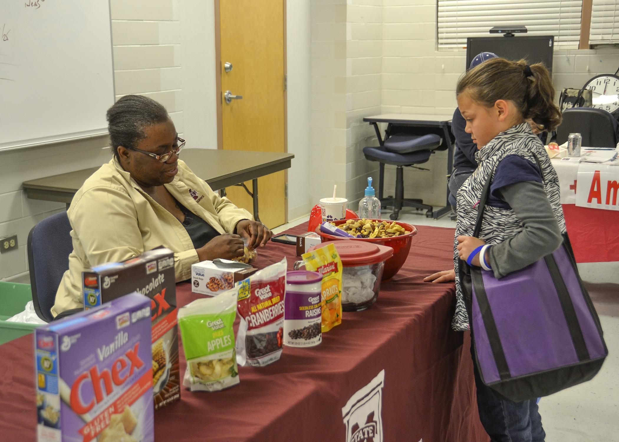 Mississippi State University Extension Service Child and Family Development agent Terri Thompson, left, gives Isabella Cornish a sample of an easy-to-make snack mix. The MSU Extension Service was one of several organizations participating in the Super Saturday healthy cooking event in Pascagoula, Mississippi on Nov. 15, 2014. (Photo by MSU Extension Service/Susan Collins-Smith)