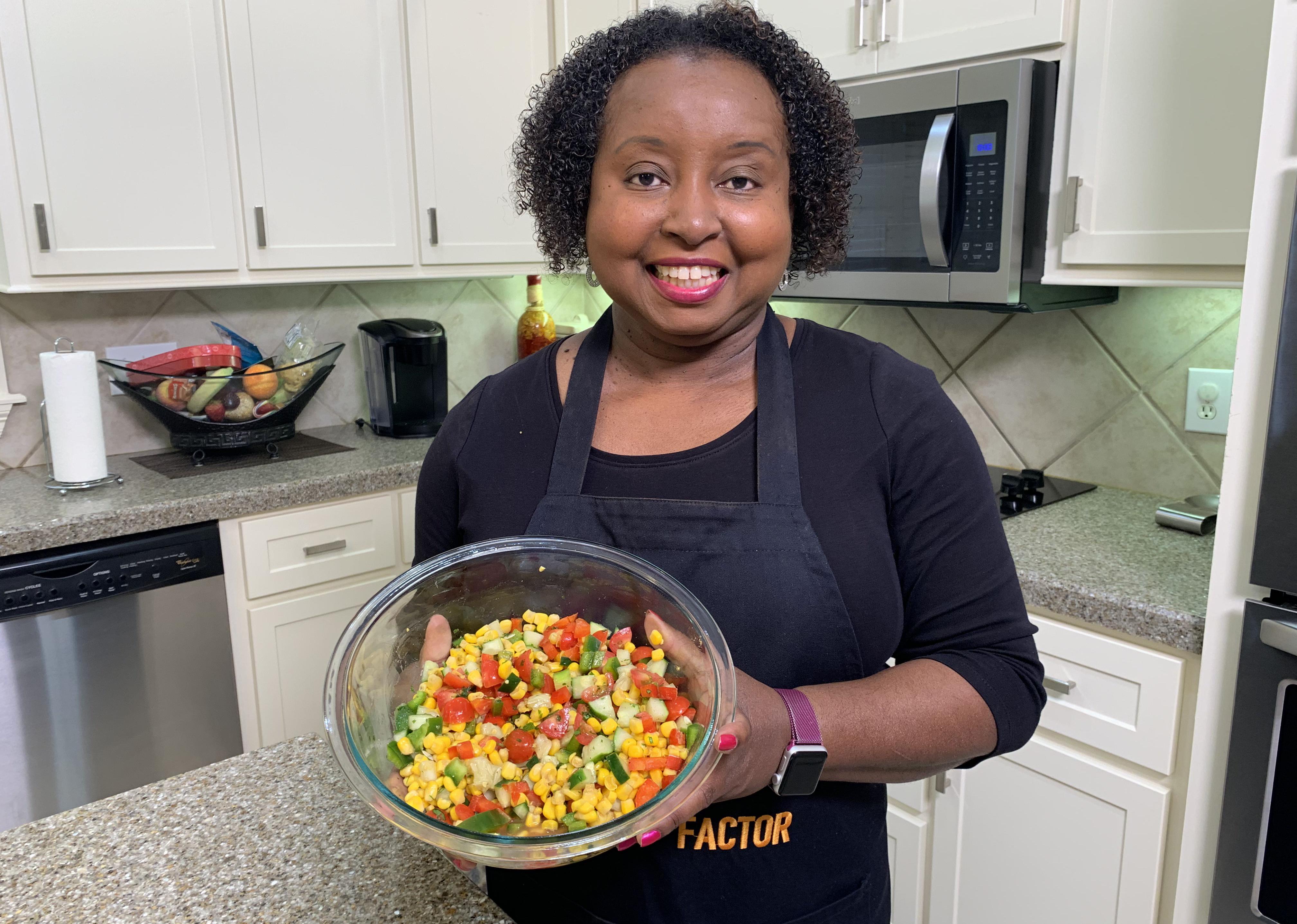 A woman holds a bowl of corn and cucumber salad.