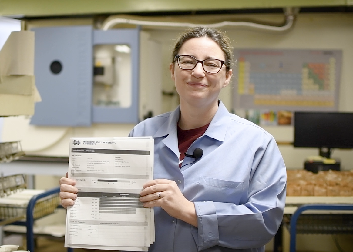 Woman in blue lab coat holding up paper.