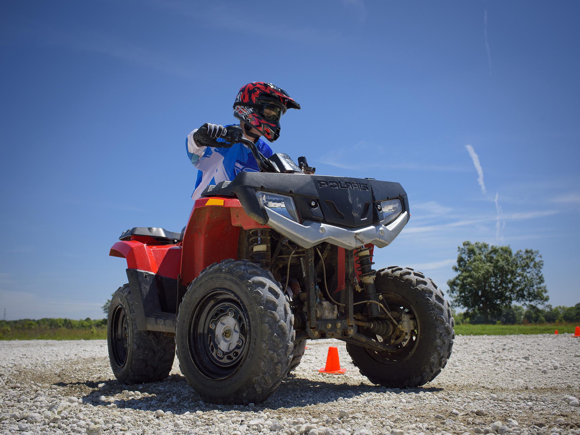 A young rider in full safety gear navigates a turn on an all-terrain vehicle.