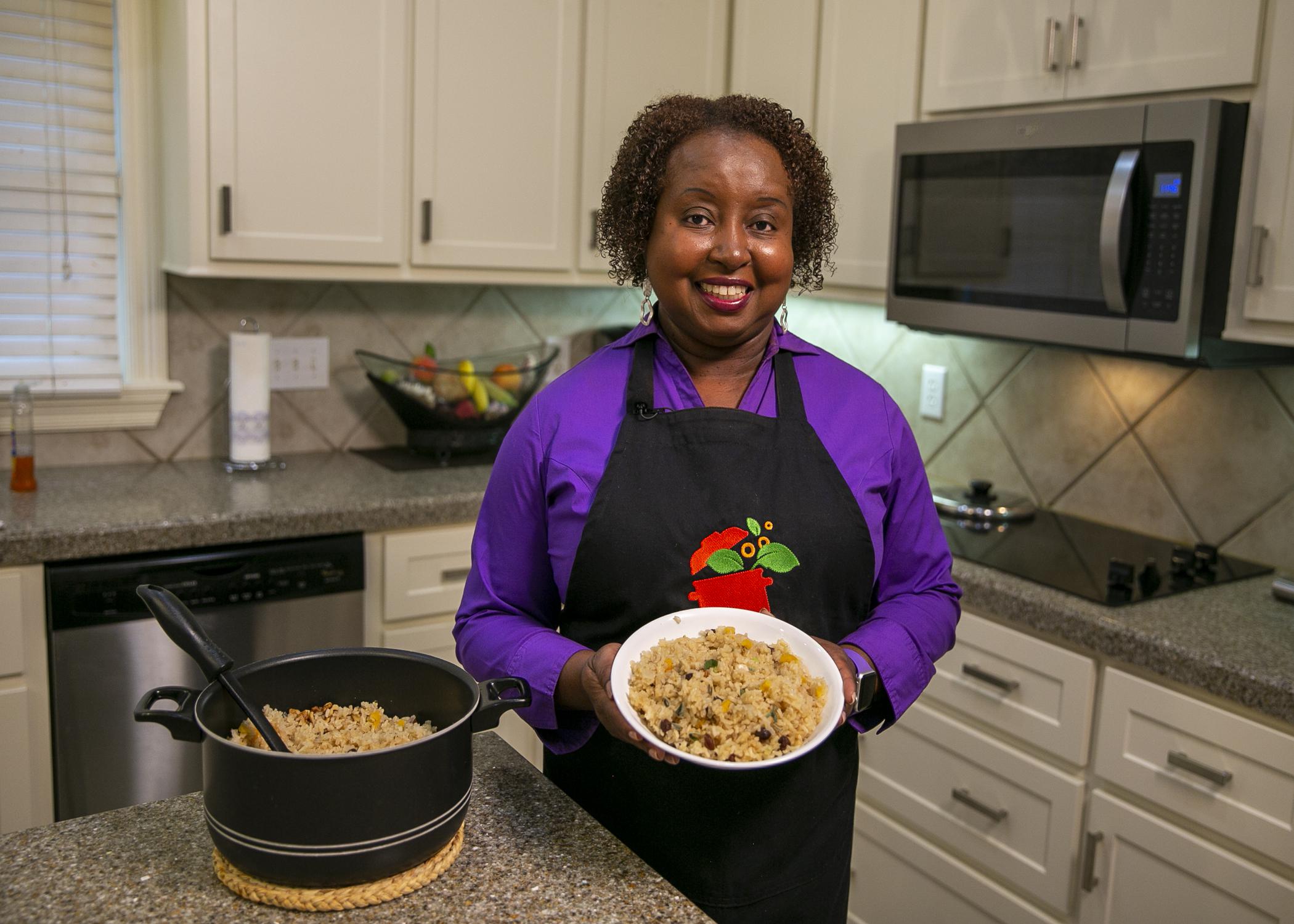 A woman stands in a kitchen with a bowl of rice pilaf posing for the camera.