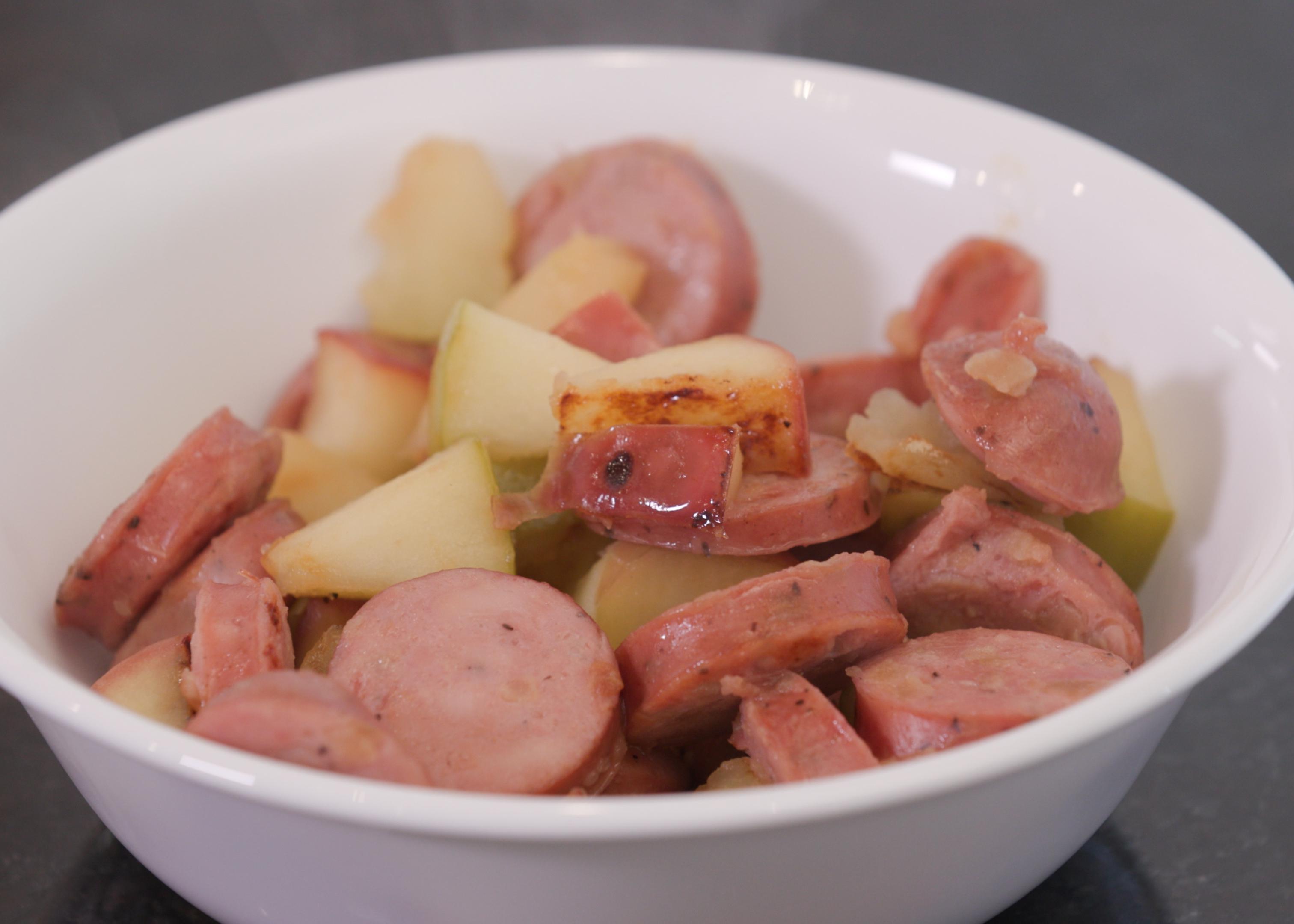 A bowl of cooked sausage and apples.