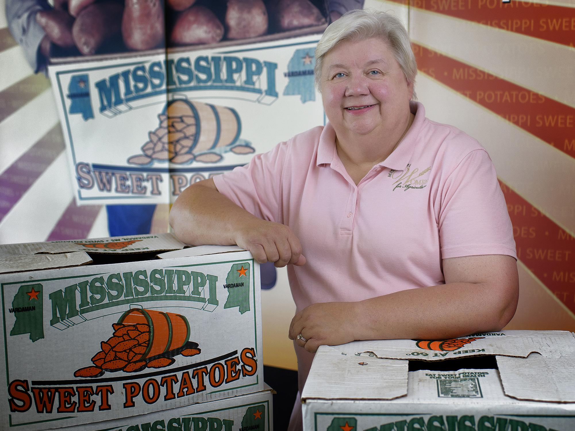 Woman pictured with arms resting on boxes labeled “Mississippi Sweet Potatoes.”