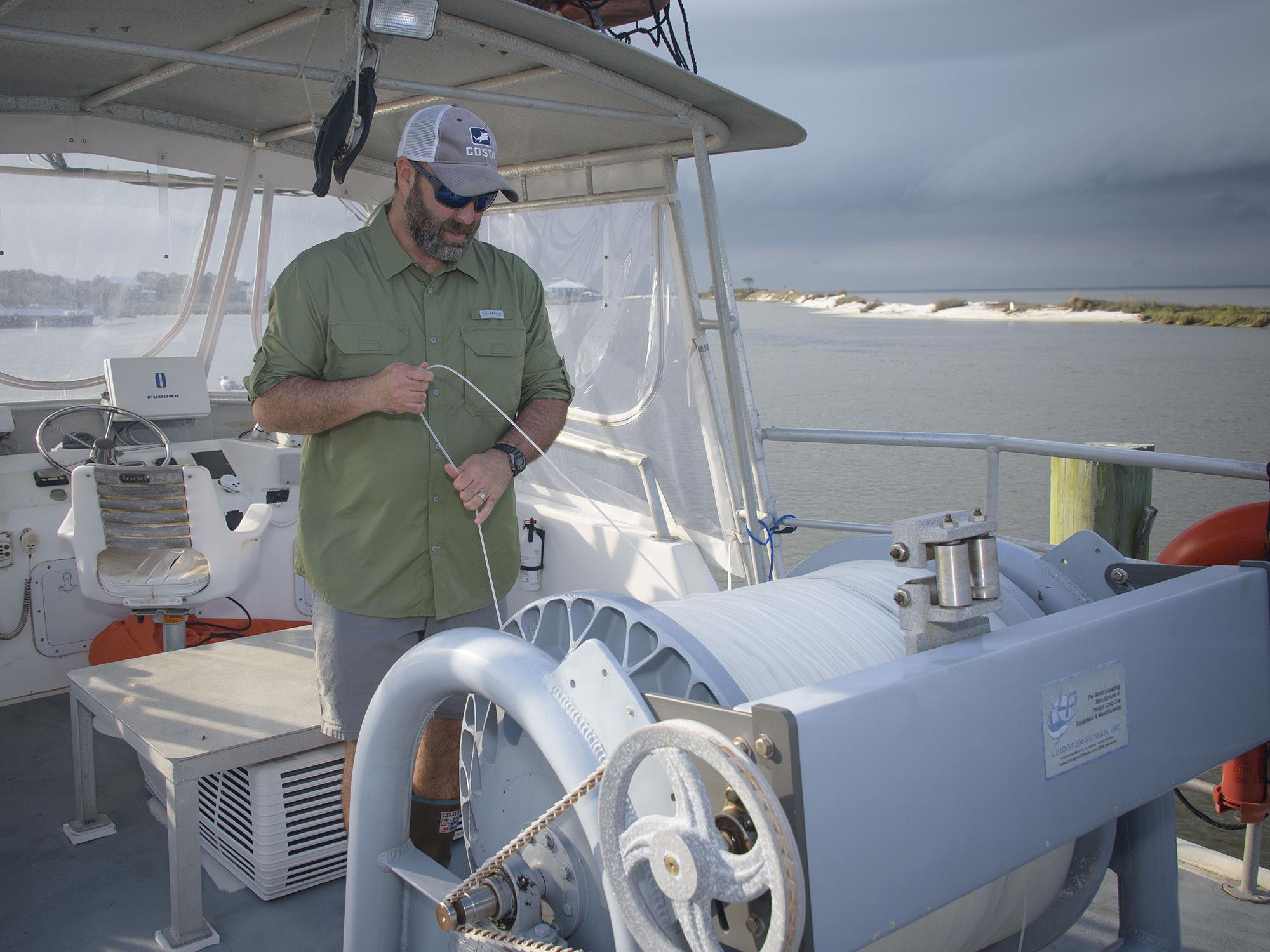 A man stands on a boat and checks a large roll of fishing line.