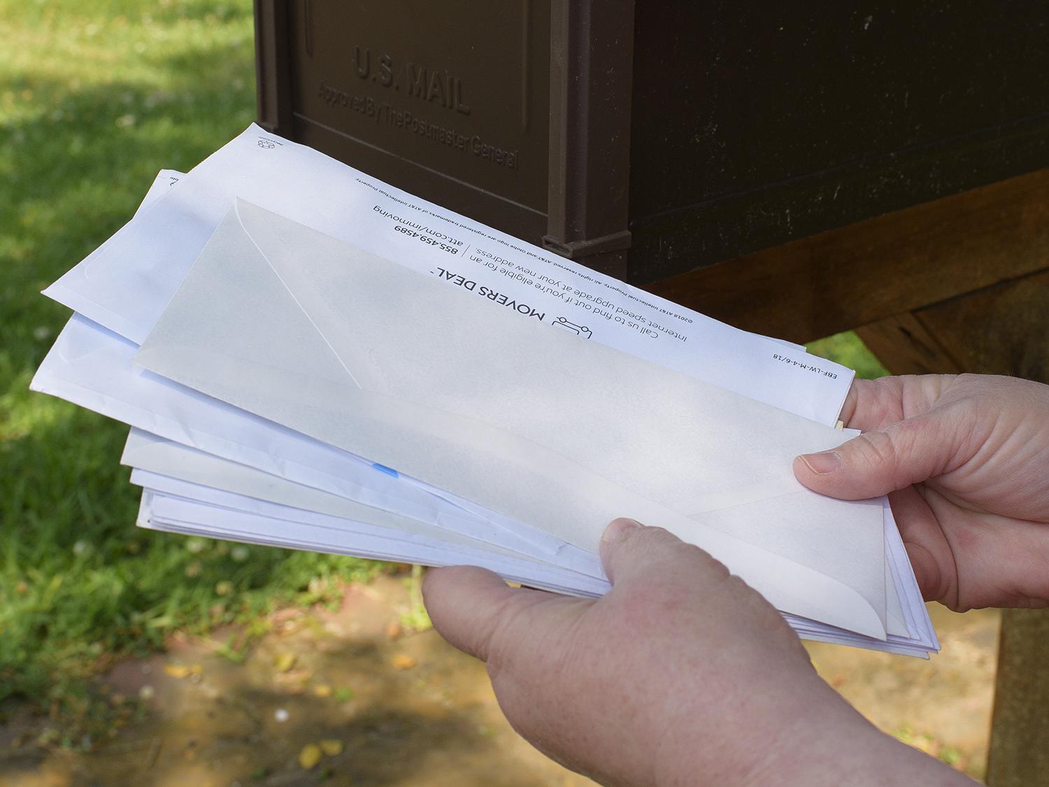 A pair of hands holds a stack of mail taken from a mailbox.